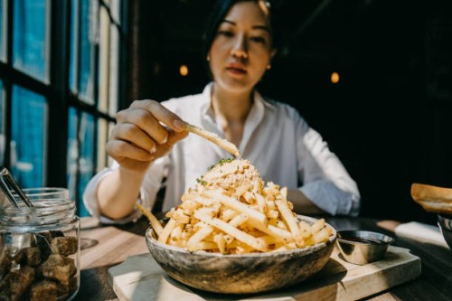 young woman sitting by the window in restaurant enjoying french fries and meal - junk food stock pictures, royalty-free photos & images