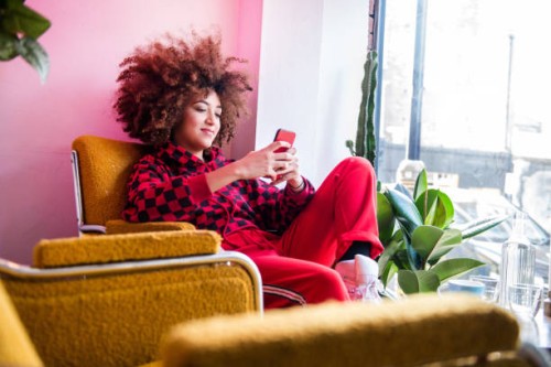 young woman sitting indoors, using smartphone - fashion stock pictures, royalty-free photos & images