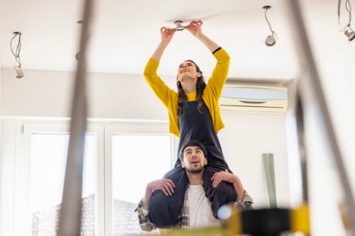 young woman sitting on boyfriend shoulders installing light bulb in new home - home decoration stock pictures, royalty-free photos & images