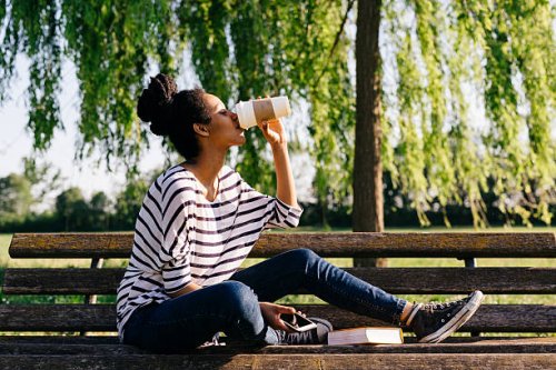 young woman sitting on park bench drinking coffee to go - junk food stock pictures, royalty-free photos & images