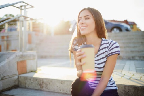 young woman sitting on stairs outdoors and holding coffee - junk food stock pictures, royalty-free photos & images