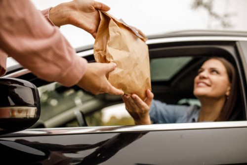 young woman smiling at service person at the drive through while receiving her takeaway order - junk food stock pictures, royalty-free photos & images