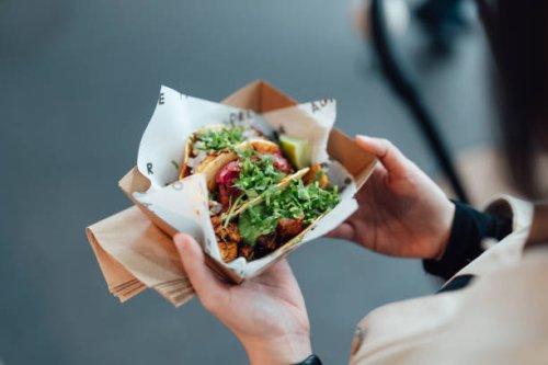 young woman taking lunch break and enjoying tacos in street food market - junk food stock pictures, royalty-free photos & images