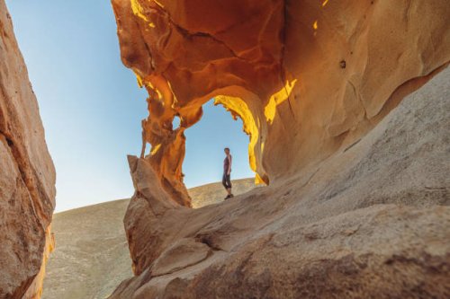 young woman under a natural rock arch in the fuerteventura desert at sunset - travel stock pictures, royalty-free photos & images