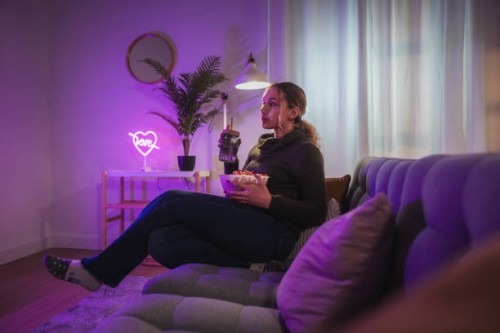 young woman watching tv and eating popcorn in cozy living room with neon lights - home decoration stock pictures, royalty-free photos & images