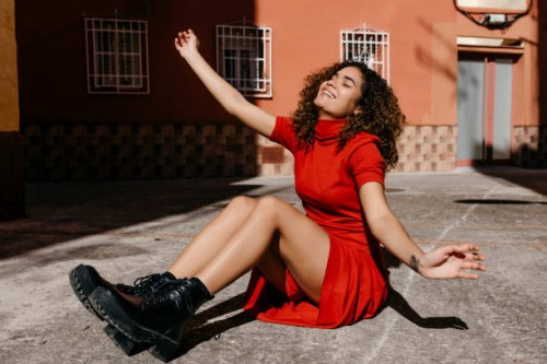 young woman wearing red dress and sitting on ground - fashion stock-fotos und bilder