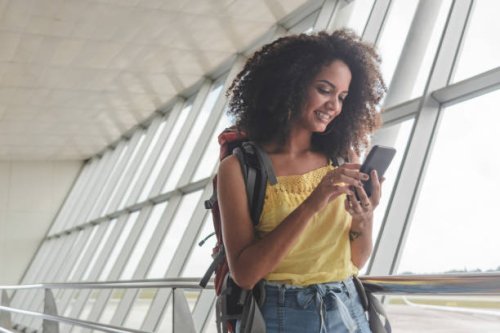 young woman with backpack checking her boarding schedule at the airport - travel stock pictures, royalty-free photos & images