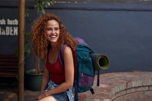 young woman with backpack smiling, while sitting in courtyard - travel stockfoto's en -beelden