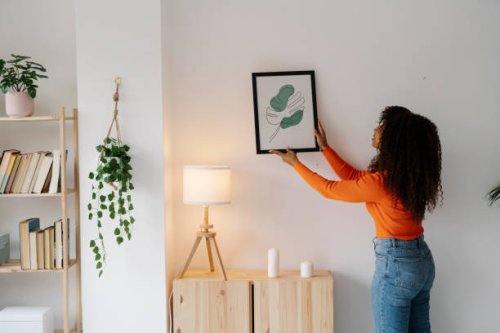 young woman with curly hair hanging picture frame on wall at home - home decoration stock pictures, royalty-free photos & images