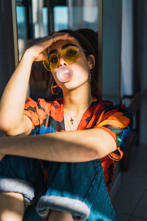 young woman with head in hand blowing bubble gum at home - fashion stock-fotos und bilder