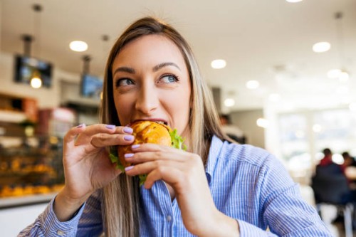 young women eating sandwich looking through window - junk food stock pictures, royalty-free photos & images