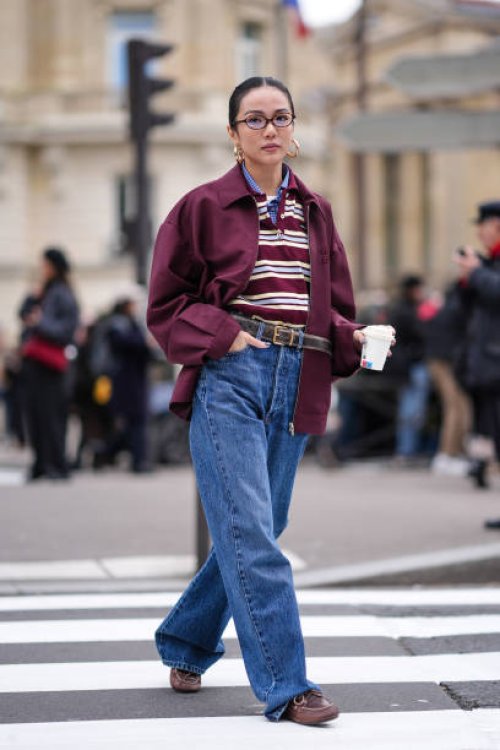 Yoyo Cao wears golden earrings, a burgundy oversized jacket , a striped polo shirt, a belt, blue denim pants / jeans , brown leather loafers shoes,...