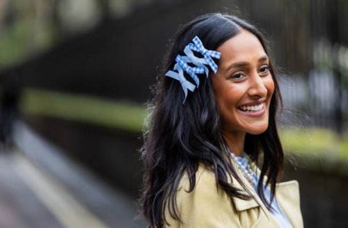 Zeena Shah wears blue bows in hair, blue dress, pearl necklace, beige coat, blue bag outside Eudon Choi during London Fashion Week February 2024 on...