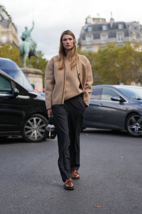 Zita D'Hauteville wears a pale / pastel brown / beige Miu Miu wool cardigan, a pullover, black pants, a black leather bag, brown leather shoes ,...