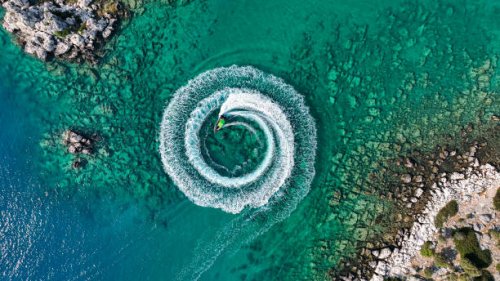 zoom out amazing aerial view of man driving a personal watercraft in the ocean creating a straight down circular pattern,amazing summer background, water color and beautiful bright clear turquoise adventure day on tropical be