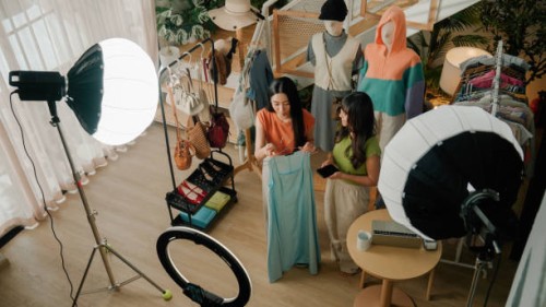 zwei junge asiatinnen präsentieren dem publikum ein kleidungsstück, während sie live für ihren online-shop verkaufen. - fashion stock-fotos und bilder